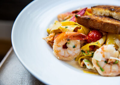 Seafood Pasta Dish. Succulent crab and shrimp tossed with pasta, tomatoes and herbs. Toasted, buttered bread on top. In a white shallow bowl.